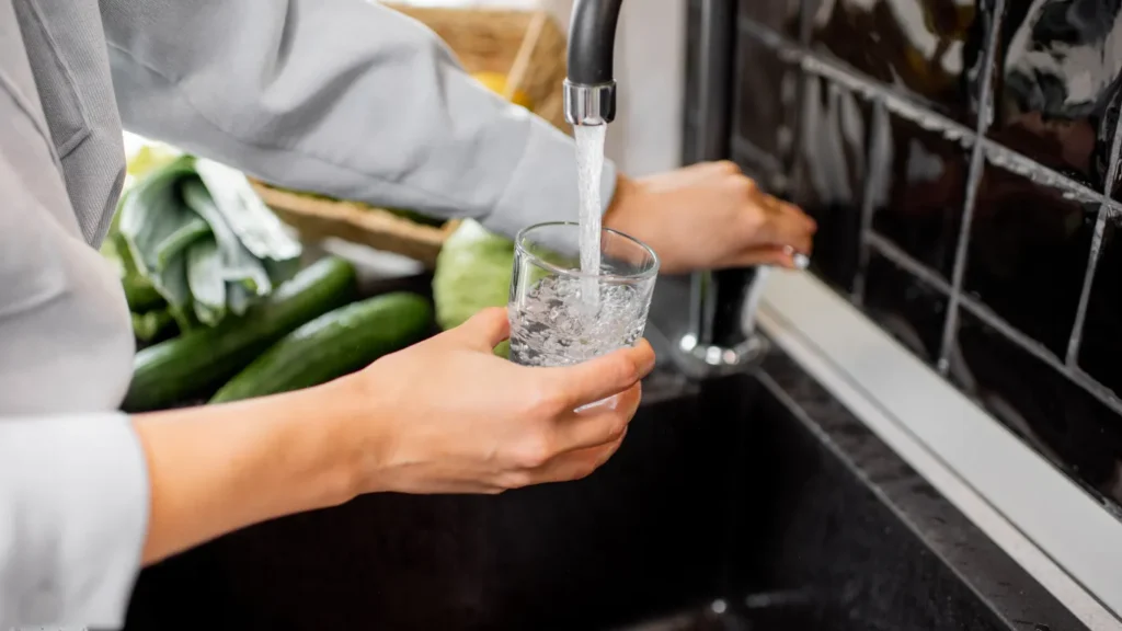 Lady filling a glass of water from the tap without any filter which will consist of harmful chemicals like chlorine and other heavy metals
