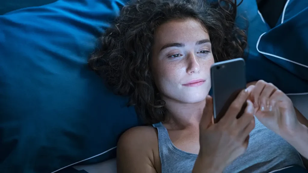 Lady using her phone during bedtime which is a toxic habit which might lead to poor sleep habits and health effects.